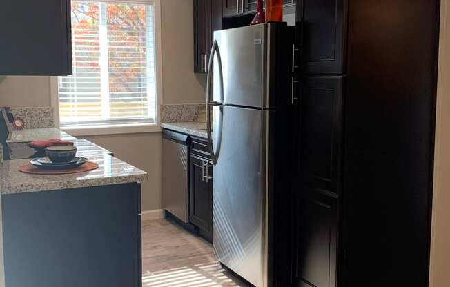 View of kitchen with brown cabinets, wood like flooring, stainless appliances, and well lit window in kitchen