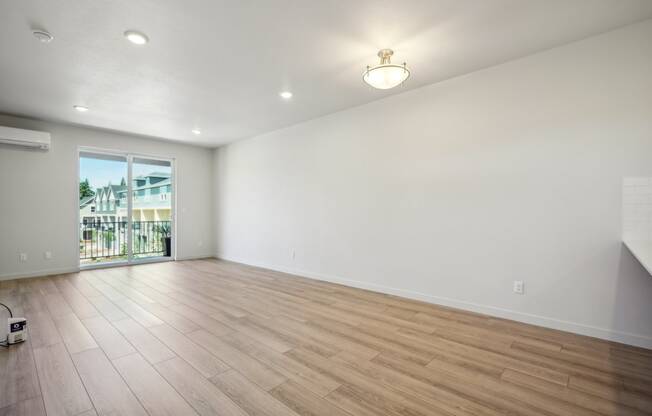 the living room is spacious and has a large window and hardwood flooring