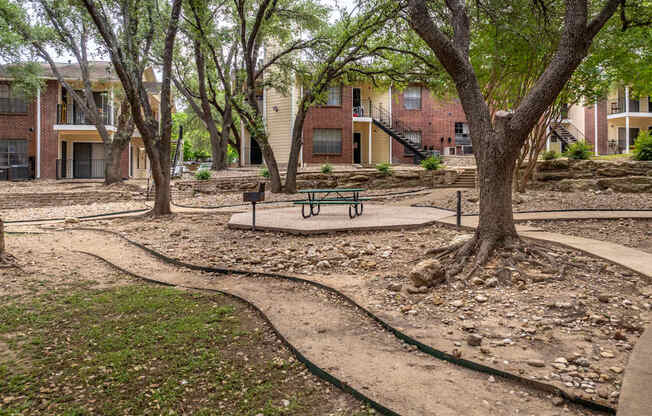 A park with a bench and a tree in front of apartment buildings.
