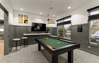 A pool table is in the middle of a room with a bar and stools.