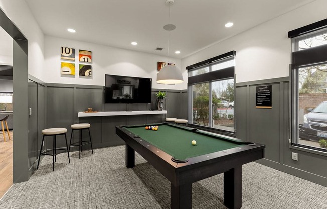 A pool table is in the middle of a room with a bar and stools.