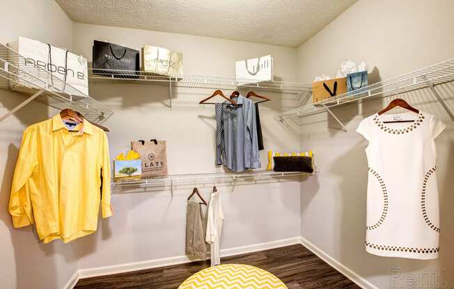 a spacious closet with shelves and clothing racks and a yellow ottoman