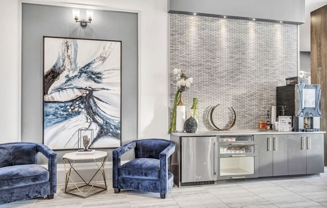 A modern living room with blue velvet chairs and a large abstract painting.