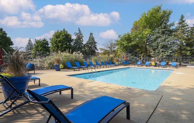 A pool surrounded by blue lounge chairs and trees.