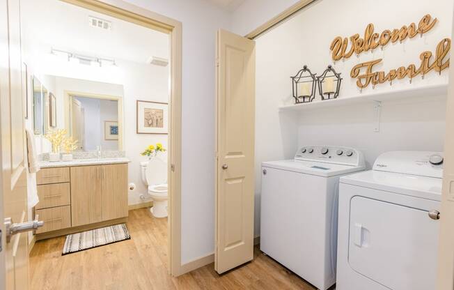 Three Bedroom Apartments in Gilbert AZ - Curve At Gilbert - Bathroom With Plank Flooring, Wood-Inspired Cabinets, A Large Vanity Mirror, And A Full-Sized In-Unit Washer And Dryer