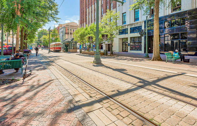 a city street with streetcar tracks and people sitting on benches