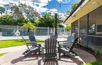 A patio with a table and chairs is surrounded by a pool and trees.