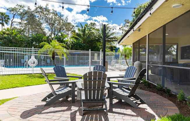 A patio with a table and chairs is surrounded by a pool and trees.