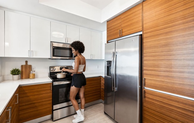 A woman is standing in a kitchen with a stove and refrigerator.
