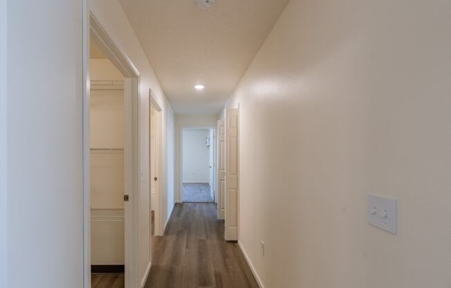 an empty hallway with white walls and wood flooring and a door to a closet. Fargo, ND Stonebridge Apartments