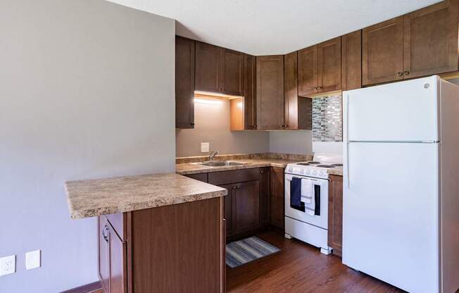 A kitchen with a white refrigerator and wooden cabinets. Little Canada, MN Montreal Courts
