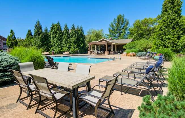 A poolside table and chairs are set up in front of a pool and a gazebo.