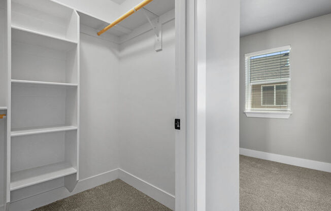 the closet in a bedroom with white shelves and a window
