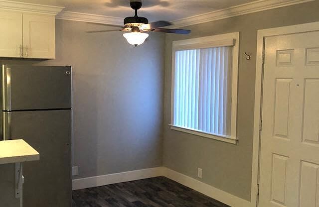 A kitchen with a refrigerator, ceiling fan, and wooden flooring.