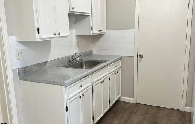 A kitchen with white cabinets and a wooden floor.