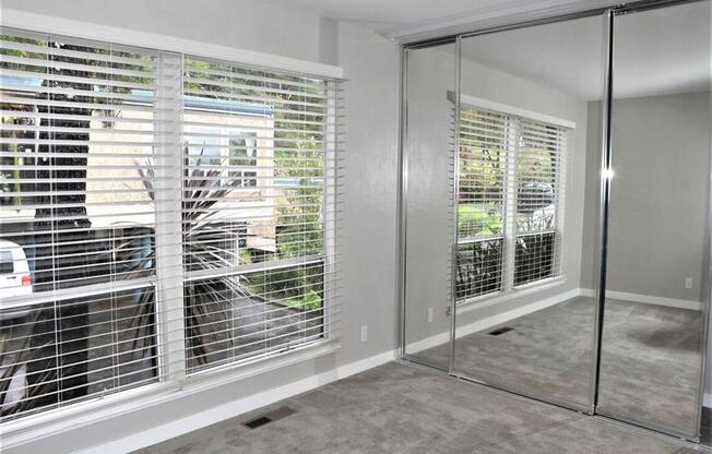 a room with a large window with blinds and a mirrored closet