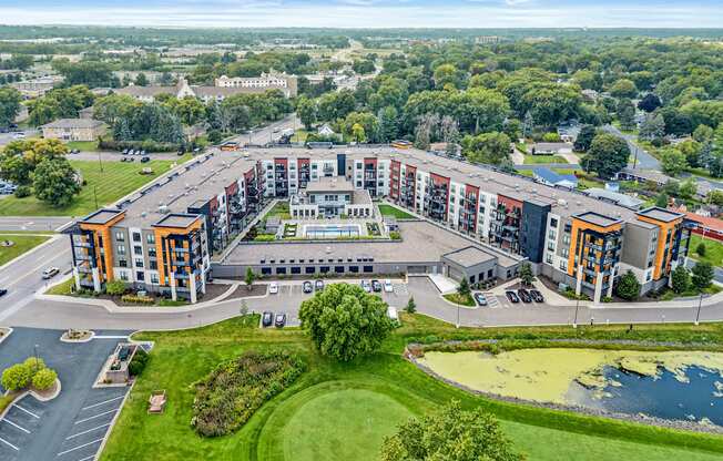A large, multi-story building with a parking lot in front and a pond in the front yard.