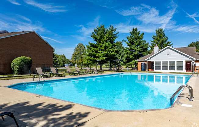 A swimming pool in front of a house with trees in the background.