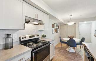 A kitchen with a stove top oven and a dining table with chairs.
