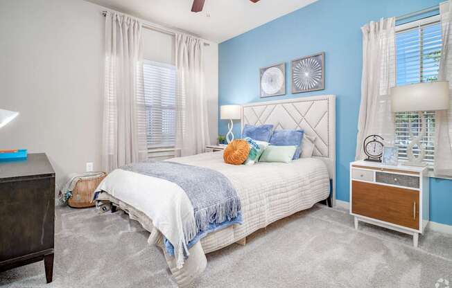 A bedroom with a white bed, blue walls, and a ceiling fan.