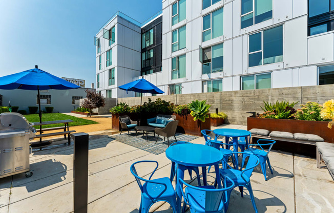 an outdoor patio with blue tables and chairs and an apartment building in the background