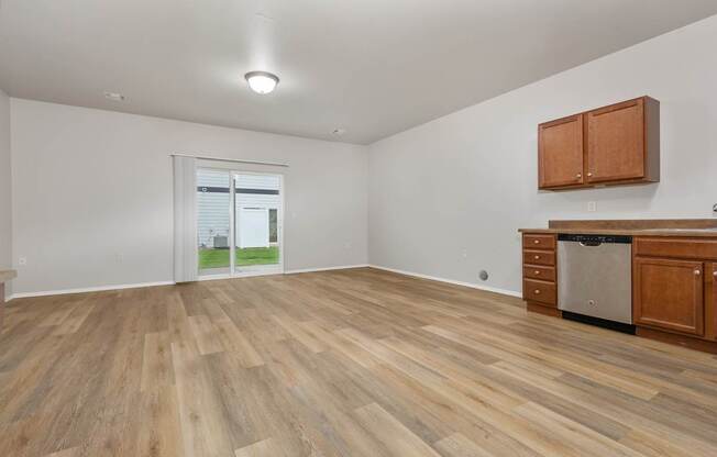 A room with wooden flooring and a window showing a view of a house.