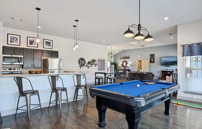a pool table in a living room with a bar and a kitchen