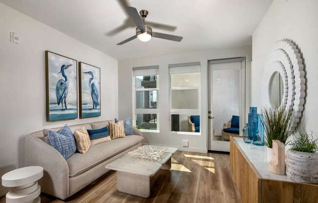 A living room with a grey couch and a painting of two birds on the wall.