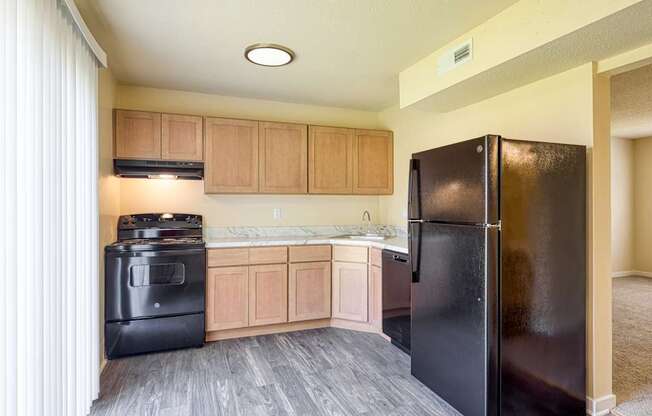 A black refrigerator is in a kitchen with wooden cabinets.