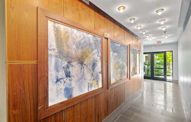 A hallway with a large painting on the wall and a glass door at the end.