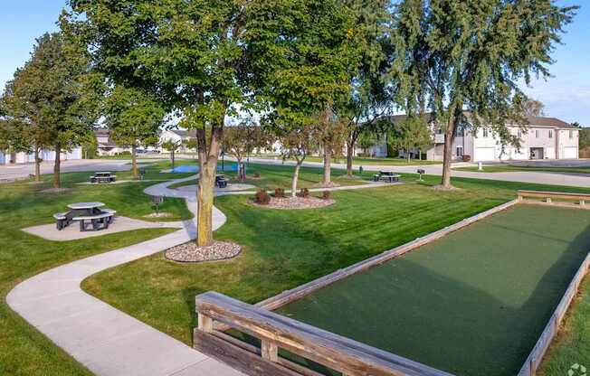 A green lawn with a small putting green and a wooden fence.