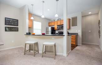 A kitchen with white walls and a white ceiling with a fridge, stove and bar stools.