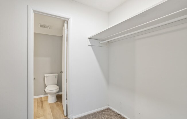 a large walk-in closet with a hanging bar and built-in shelving and bathroom access in a Mountainside Apartment