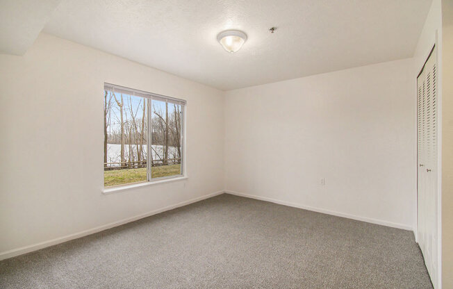 Bedroom with a large window and carpet at Canal 2 Apartments, Lansing, Michigan