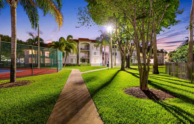 A pathway leads through a grassy area with trees and a tennis court.