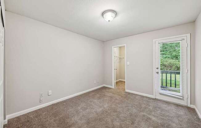 A bedroom with a carpeted floor and a door leading to a balcony at Gwinnett Square Apartments in Duluth, GA