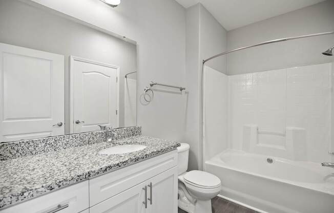 A white bathroom with a granite countertop and a white bathtub.