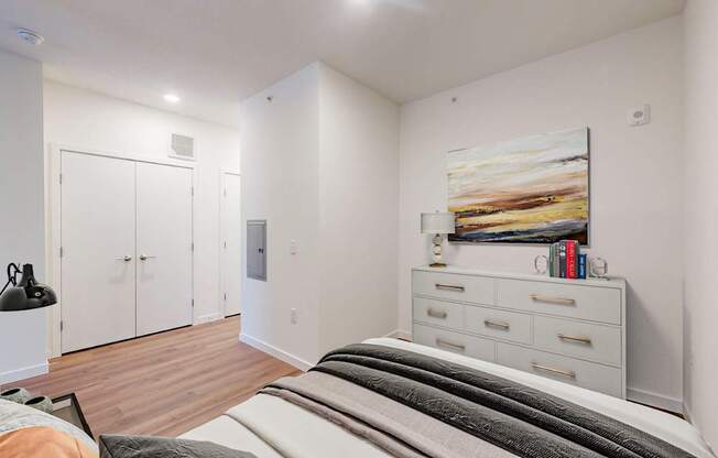A bedroom with a bed, dresser, and painting on the wall.