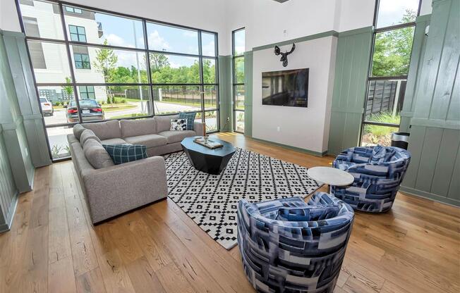 Community room with large windows, an L-shaped sofa, hard floors, chairs, and a TV