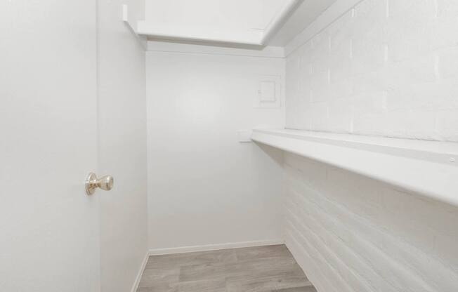 A white door with a gold handle is on the left side of a room with white walls and a white brick wall on the right side.