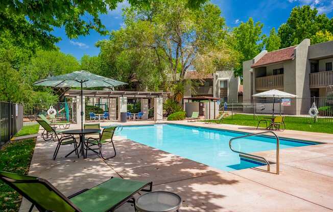 A pool area with a table and chairs and a green umbrella.