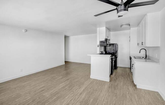 an empty living room with a kitchen and a ceiling fan