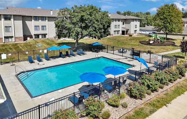 A swimming pool surrounded by a black fence and blue umbrellas.