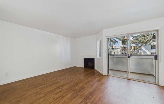 A room with wooden flooring and a window with a view of trees and buildings outside.