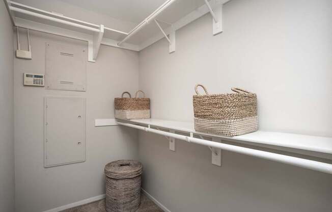 A white room with two baskets on shelves and a trash can.