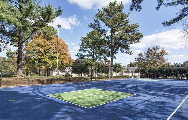 A tennis court surrounded by trees and a fence.
