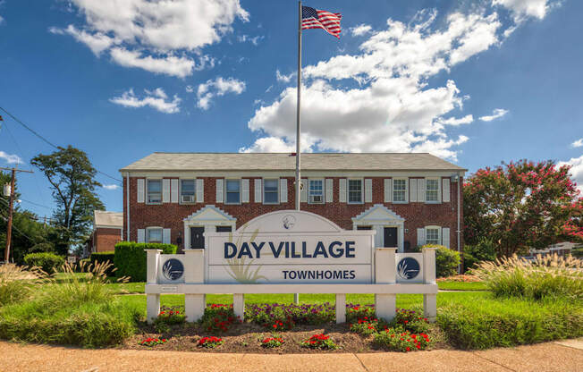 A sign for Day Village Townhomes stands in front of a brick building.