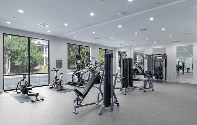 A spacious gym with a variety of equipment and a view of trees outside the windows.