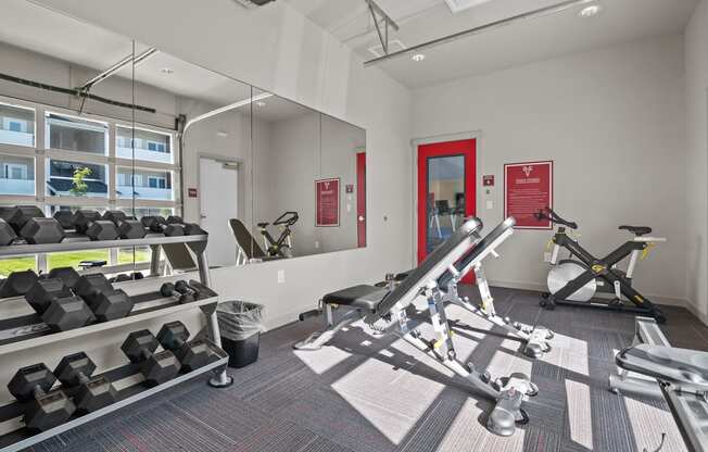a gym with weights and mirrors at the district flats apartments in lenexa