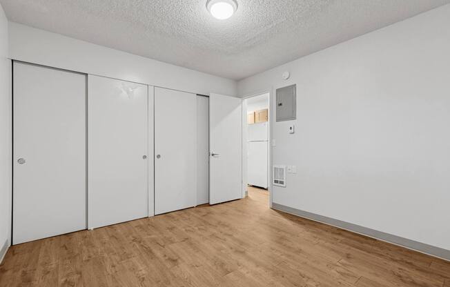 A room with white walls and wooden flooring, featuring a white door and a white closet with a mirror.